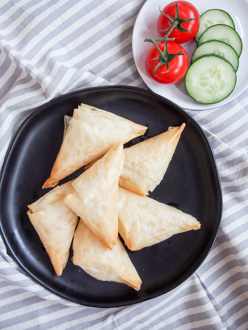 plate of tiropita Greek cheese pastries from overhead with slices of cucumber and tomatoes on plate to side