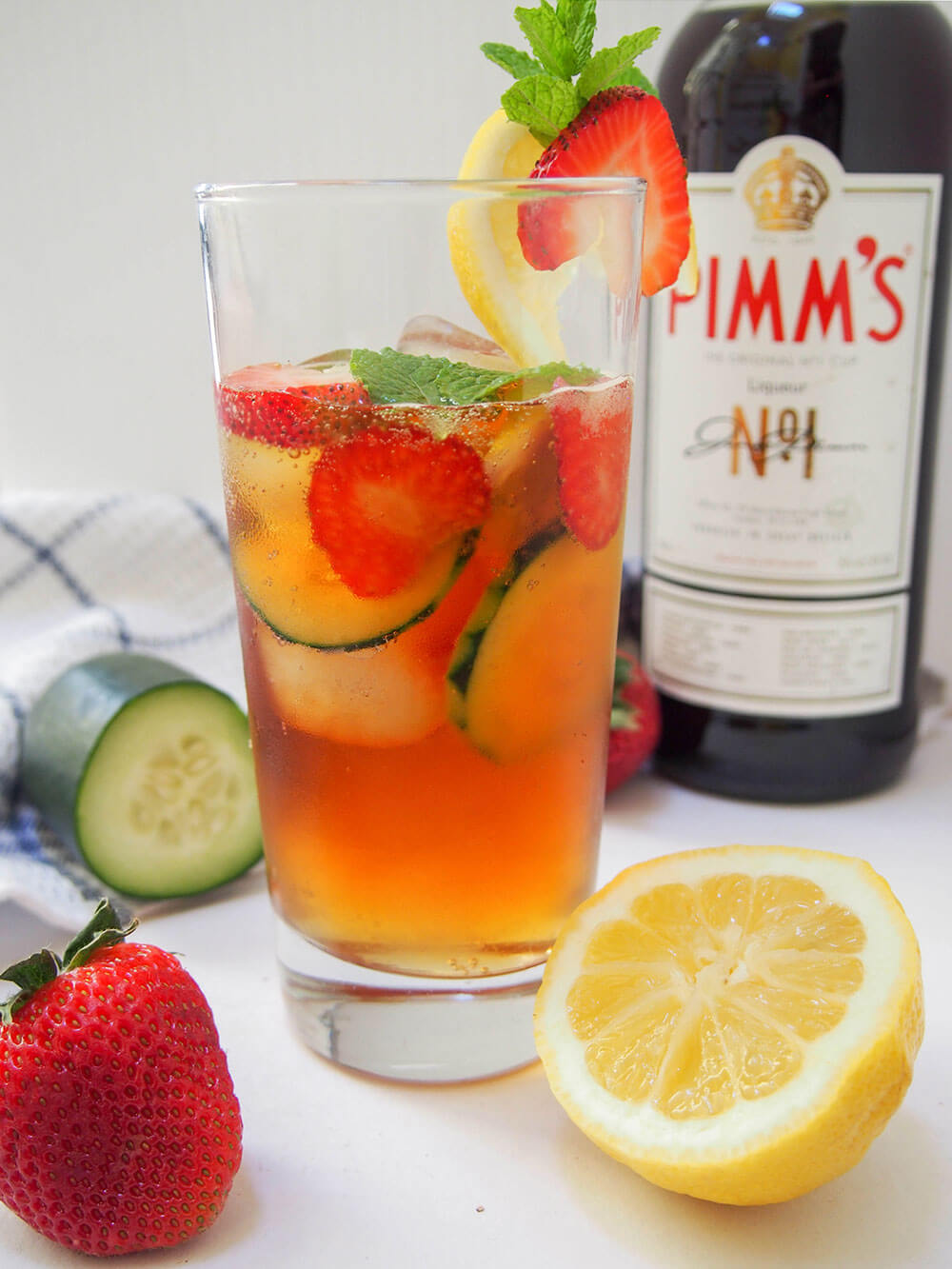 side view of glass of Pimm's cup cocktail with bottle of Pimm's behind