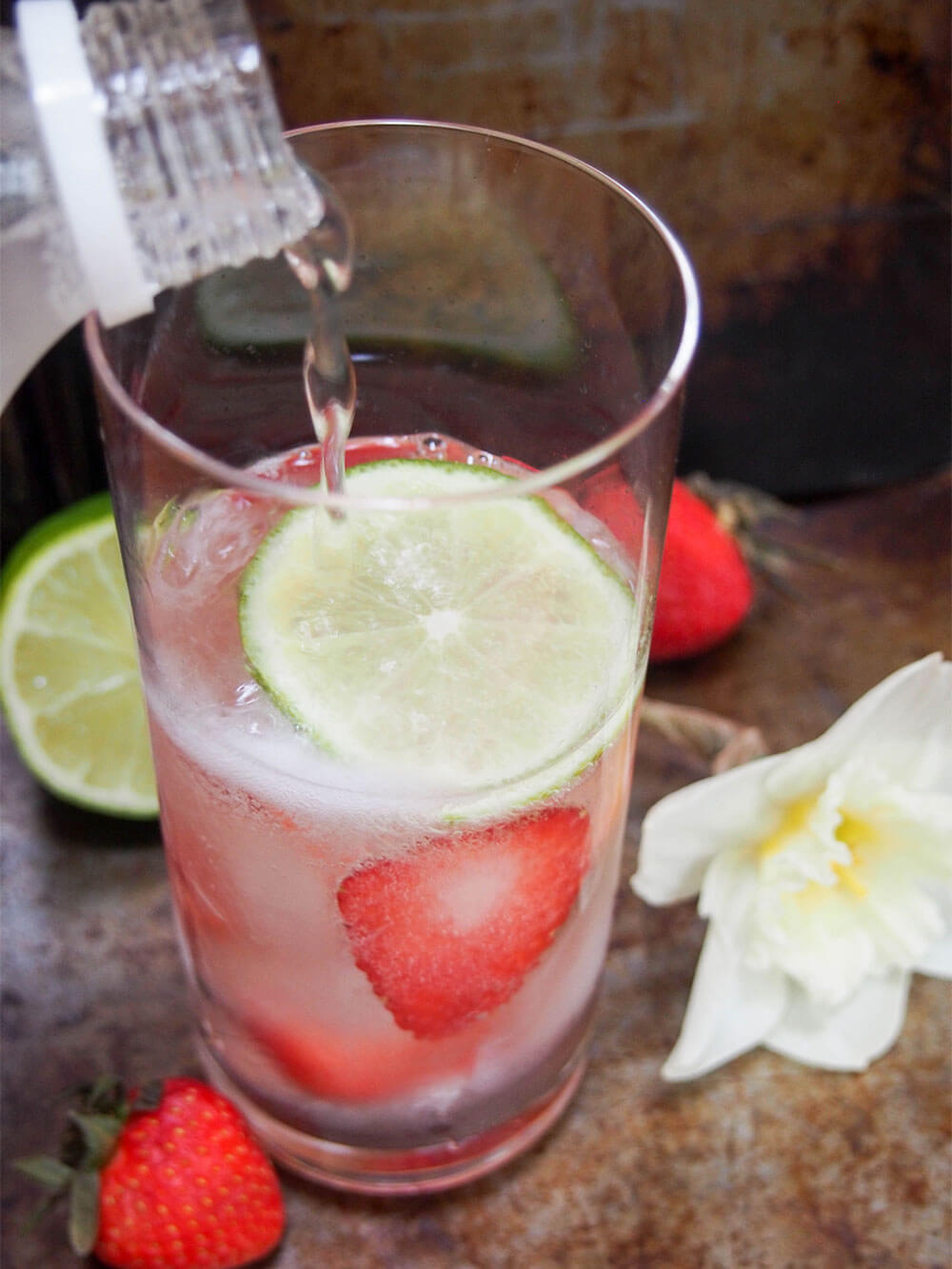 adding tonic to glass with spirits, strawberry and slice of lime