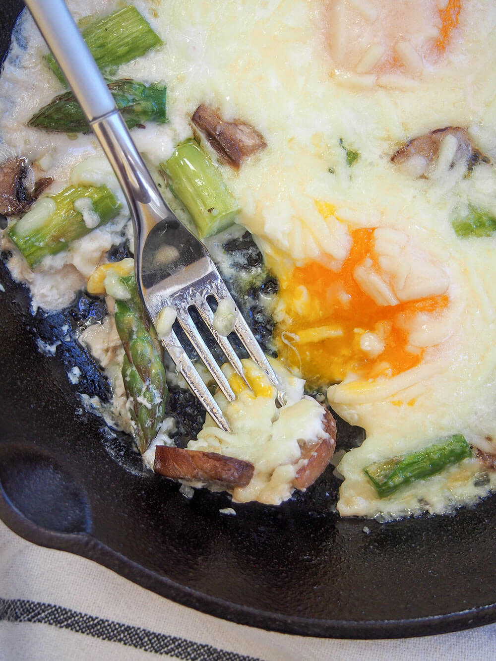 starting to eat Baked eggs with mushrooms and asparagus - fork in pan