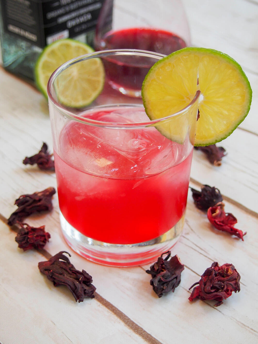 glass of hibiscus mezcal sour with slice of lime garnish and dried hibiscus flowers around glass