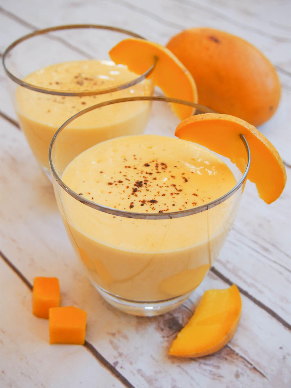 two glasses of mango lassi with a slice of mango garnishing the glasses