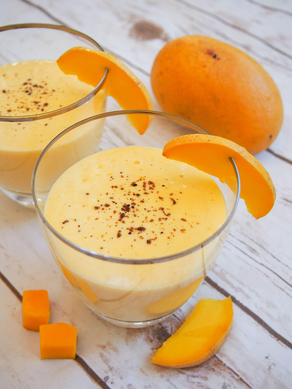 mango lassi in a glass with mango behind