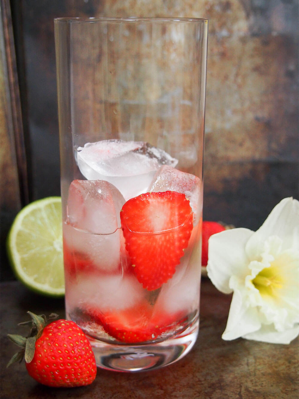 Spirits, ice and strawberries in glass before topping up