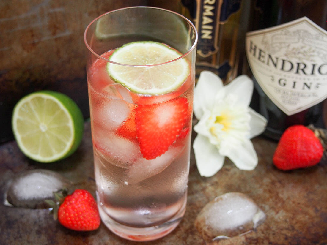 glass of strawberry St Germain gin and tonic with lime to side and bottles behind
