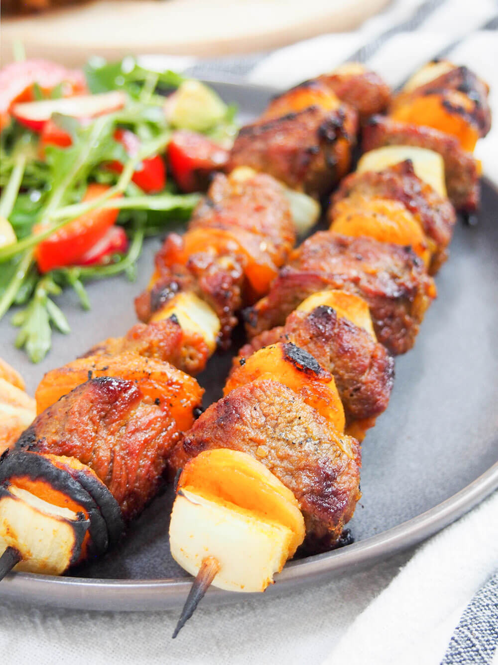 Sosaties (South African lamb and apricot kebabs) on plate with side salad behind