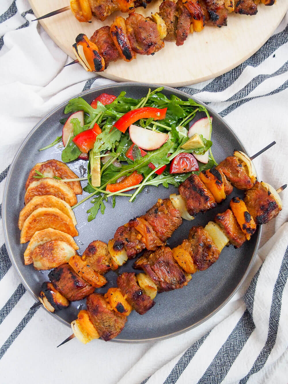Plate with two sosaties skewers (South African lamb and apricot kebabs) with salad and potatoes on side