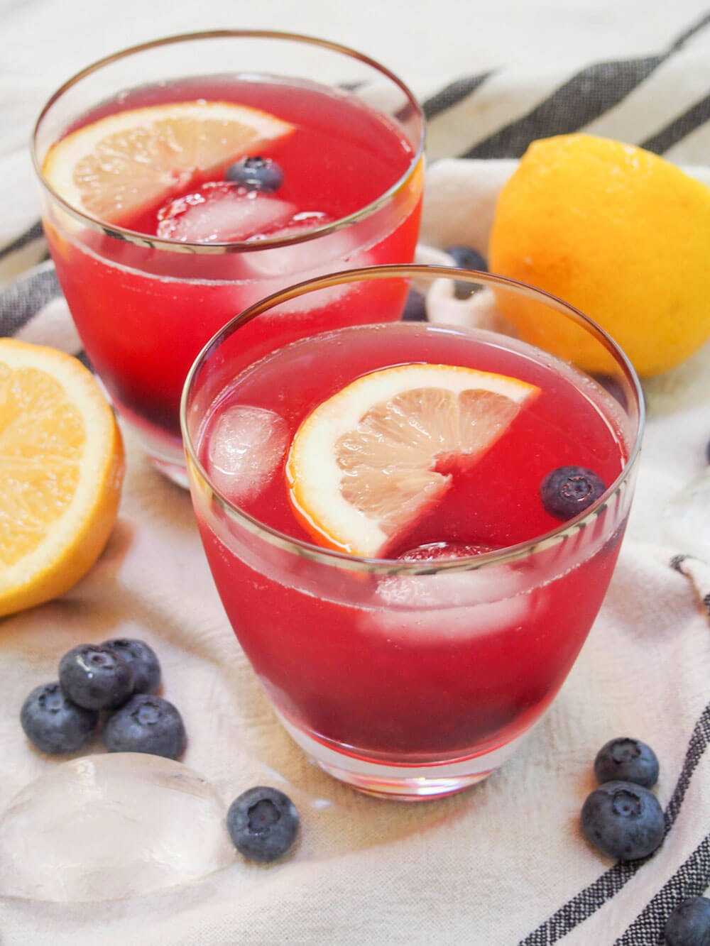 two glasses of blueberry lemonade with lemons and blueberries to side