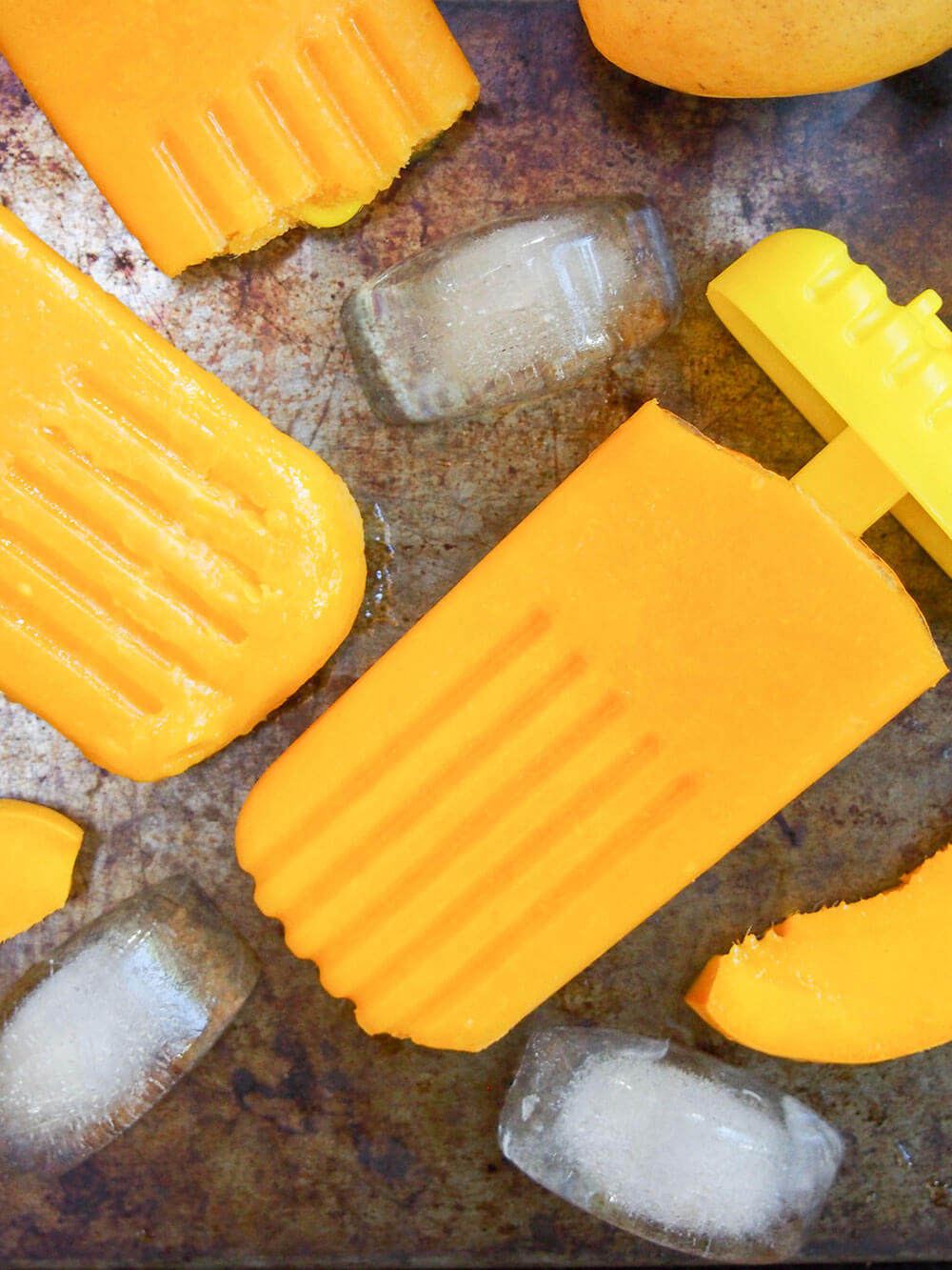 mango paletas on surface with ice cubes around from overhead