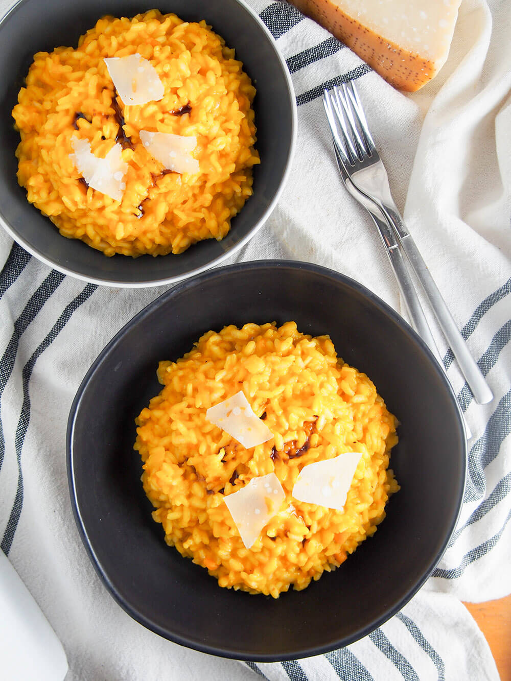 two bowls of pumpkin risotto viewed from overhead with forks to side