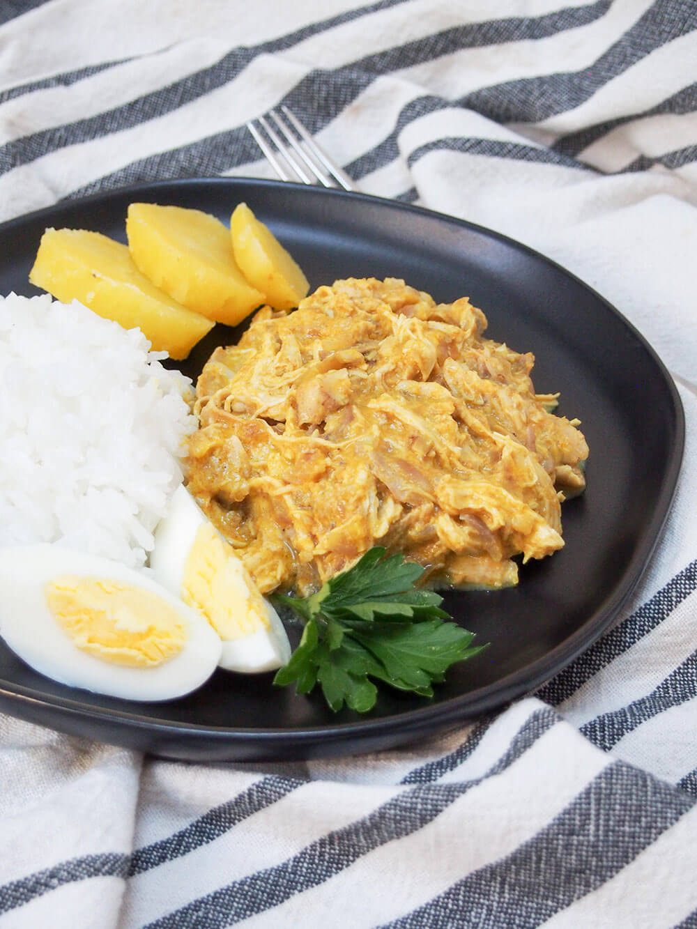 Aji de gallina (Peruvian chicken) served with traditional sides of rice, potato and egg Aji de gallina (Peruvian chicken) with rice, egg and potatoes on side, all on black plate
