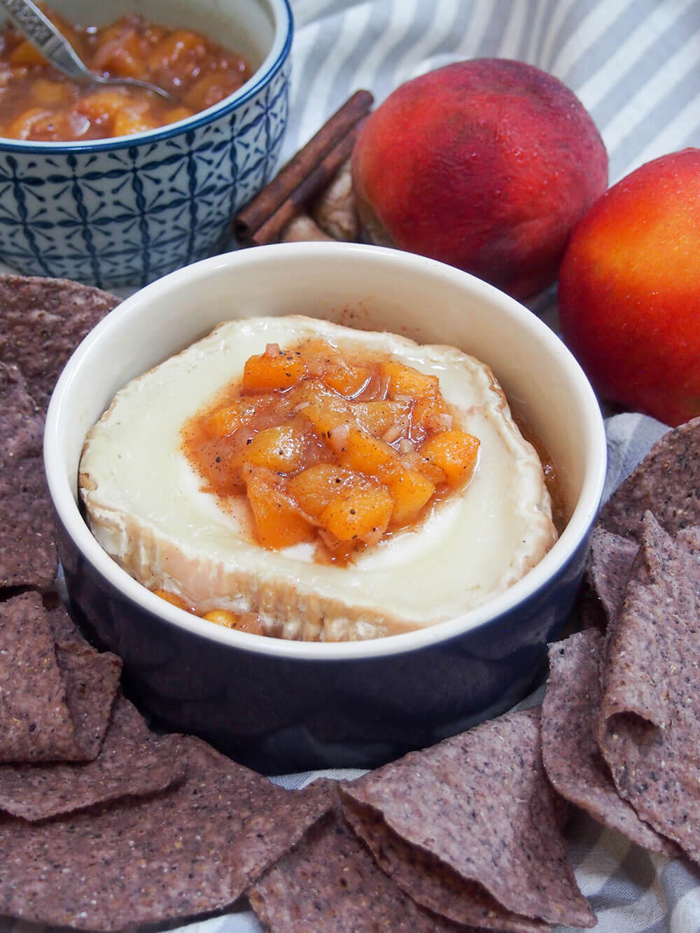baked goat cheese with peach chutney on top, with tortilla chips around bowl and peaches behind