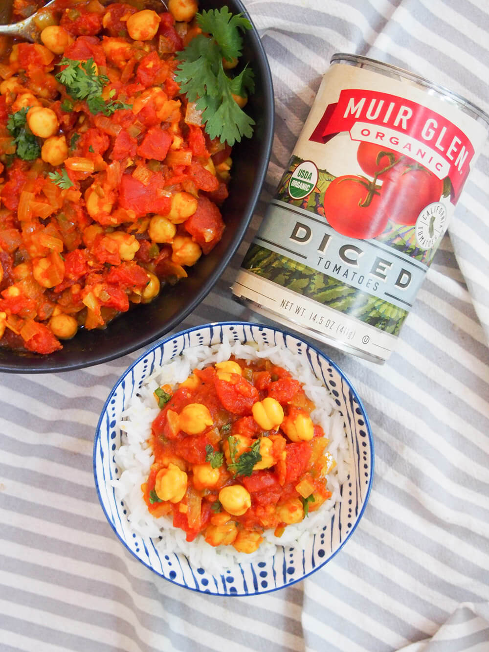 chana masala in serving bowl, over rice and with can of tomatoes to side