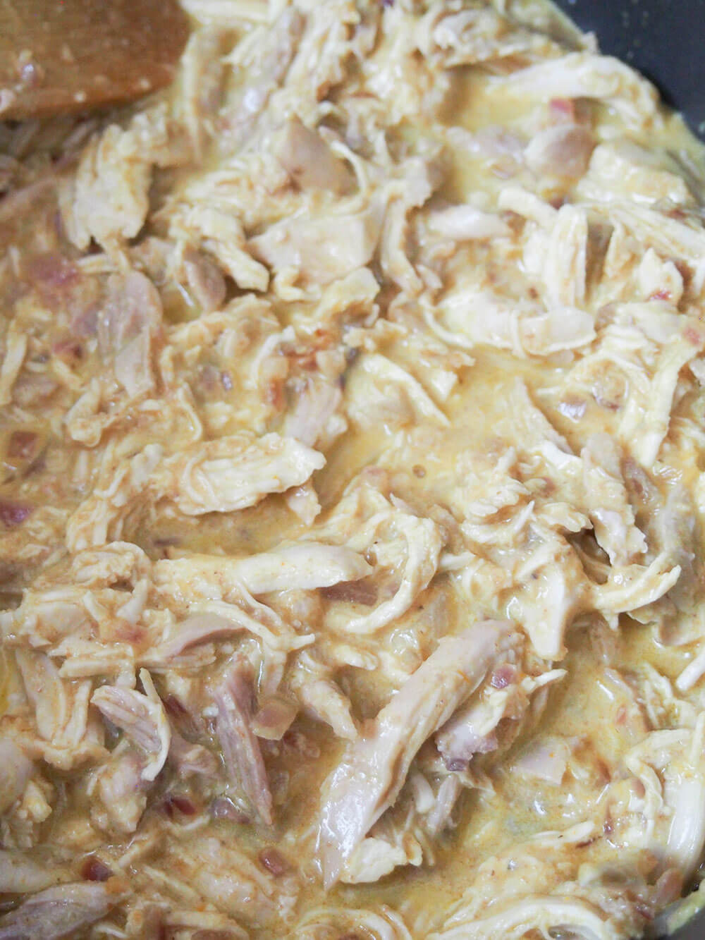 Aji de gallina is a classic Peruvian dish, with shredded chicken wrapped in a smooth, creamy sauce with chili, cheese and walnuts. Stirring aji de gallina in pot