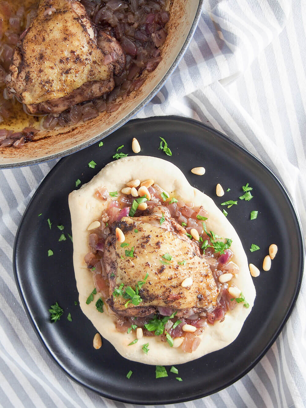 Musakhan (Palestinian sumac chicken) served on a piece of bread on plate with additional chicken in dish to side