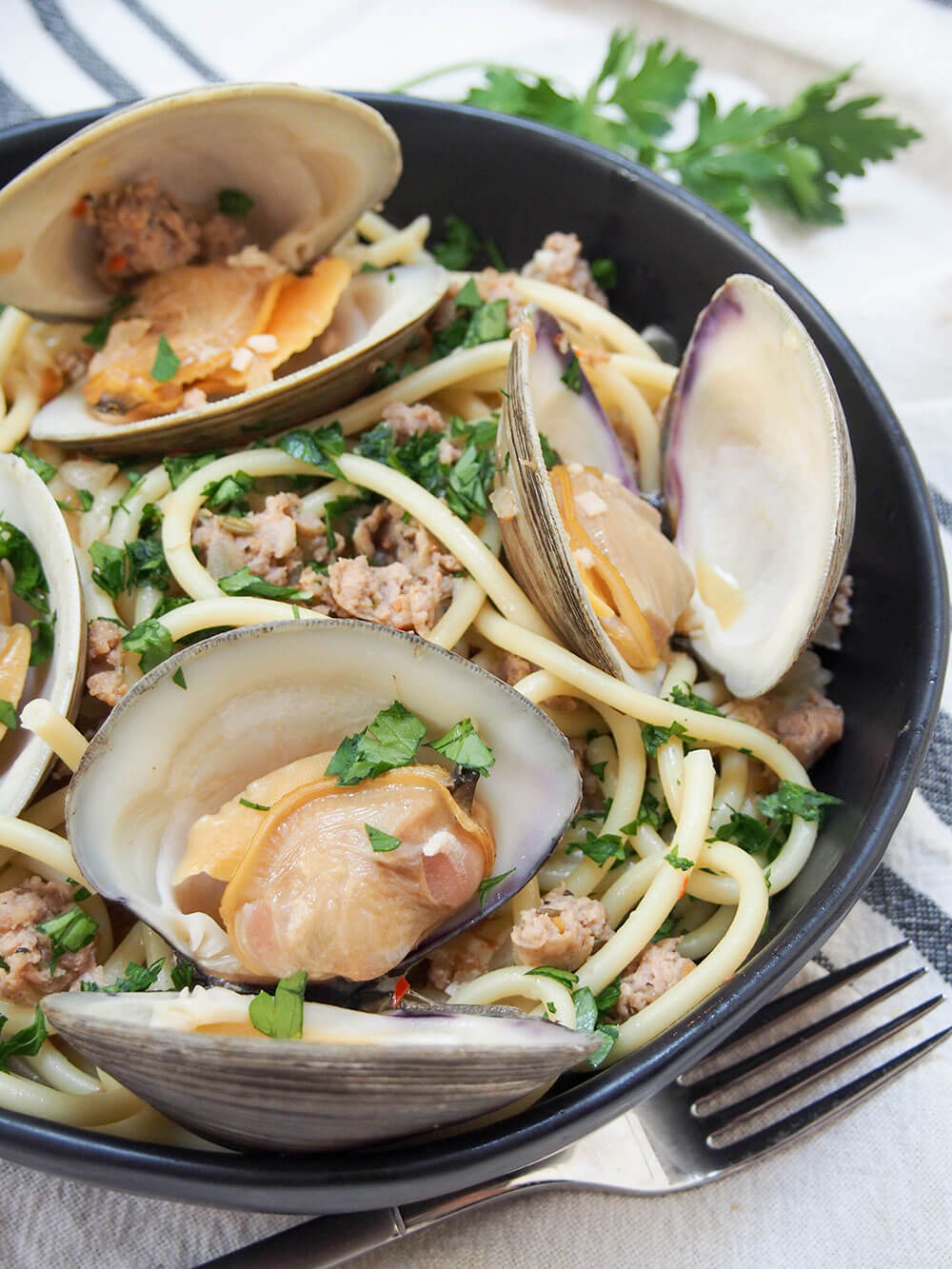 Pasta with clams and sausage in bowl with fork in front
