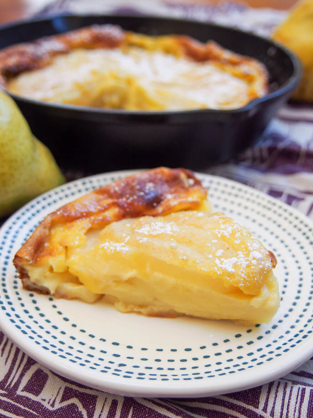 slice of pear clafoutis on plate, rest in skillet behind