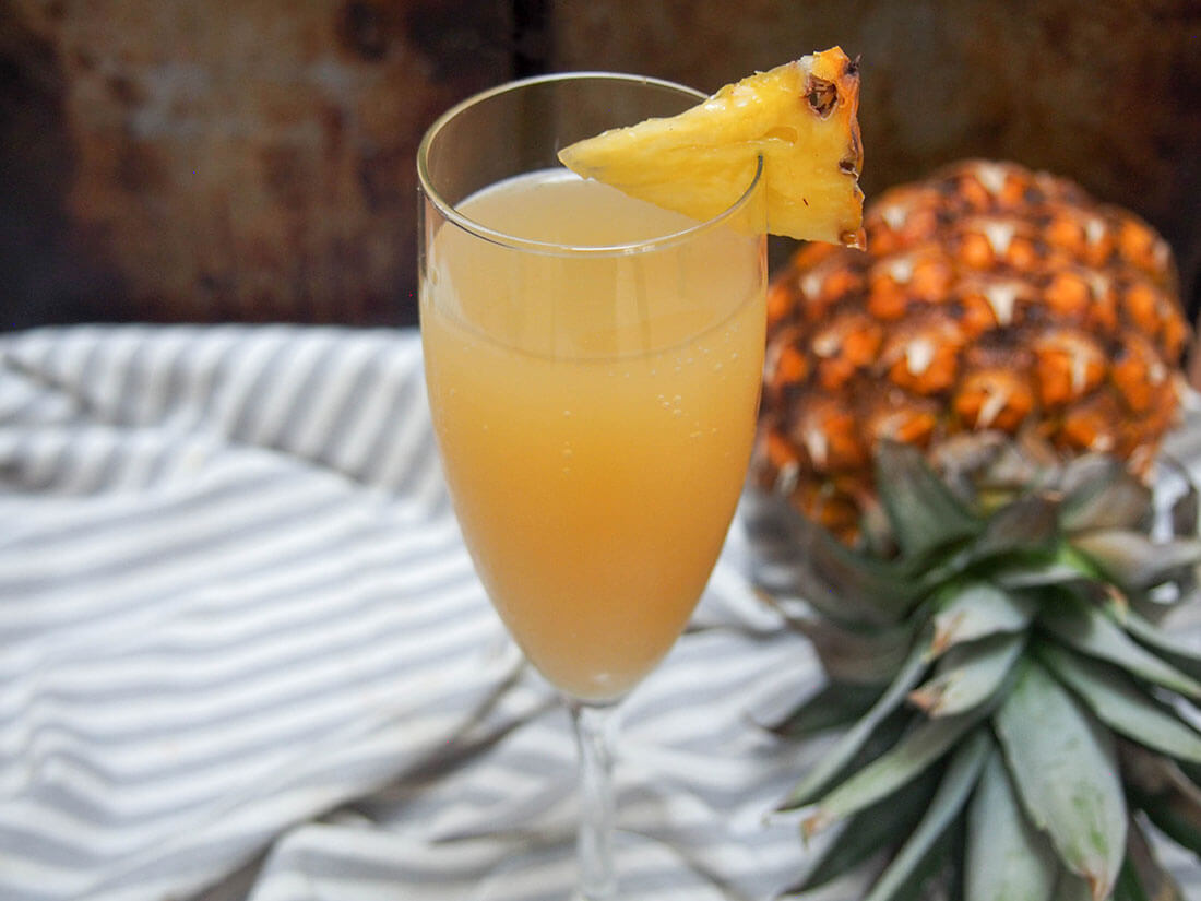 glass of pineapple mimosa with pineapple to side