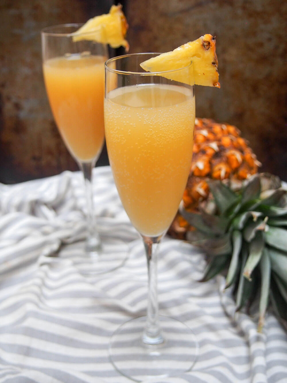 two glasses of pineapple mimosa with pineapple to side