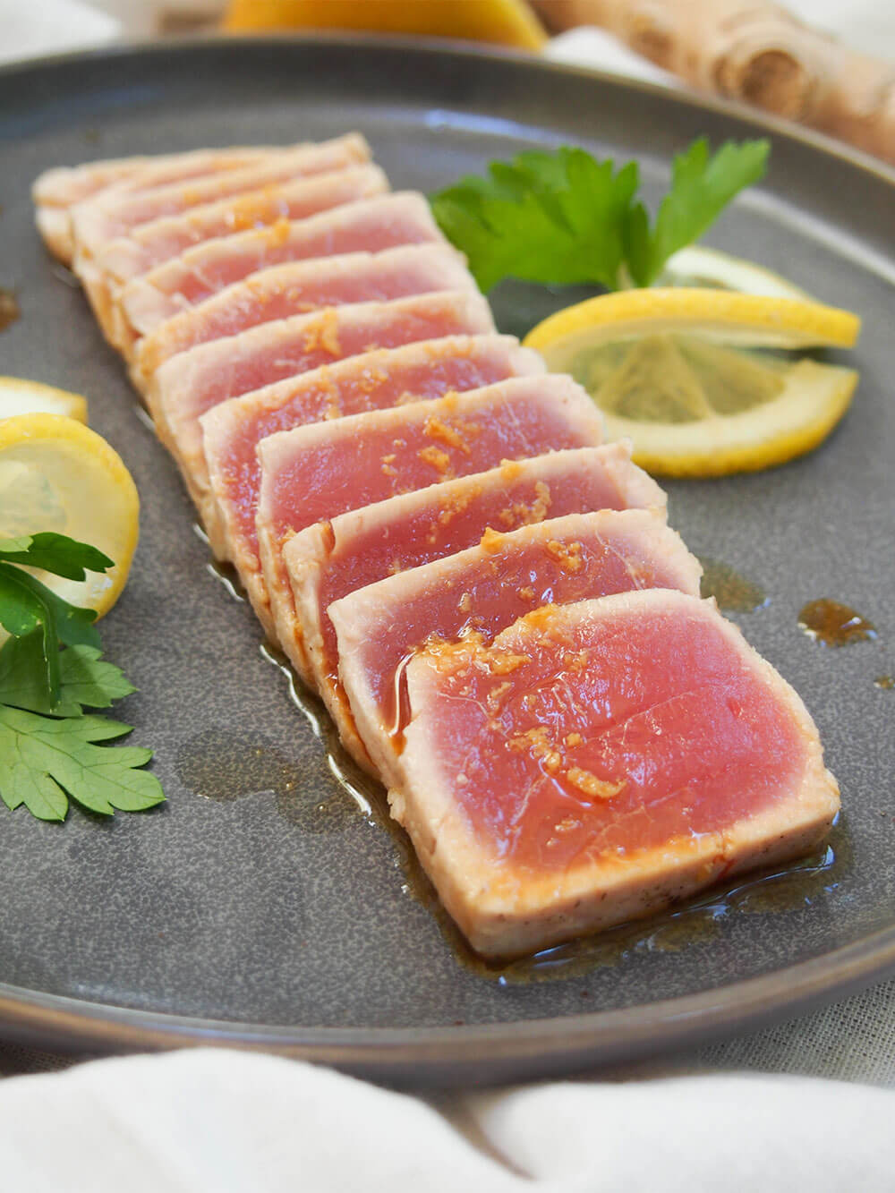 tuna tataki slices with ginger ponzu on top and slices of lemon on side of plate
