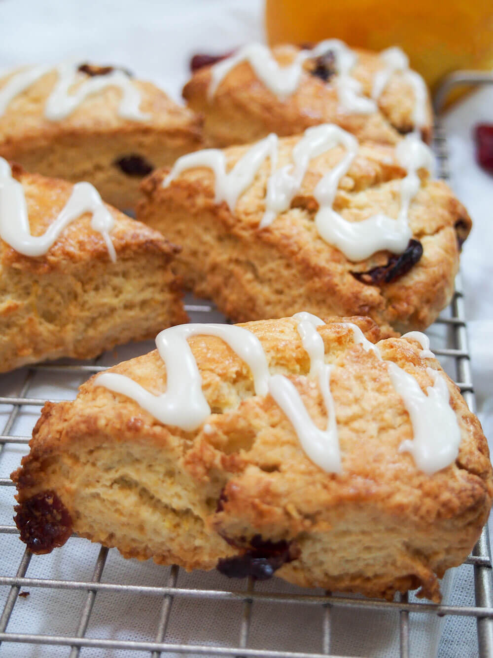 Cranberry orange scones with glaze drizzled on top, resting on cooling rack
