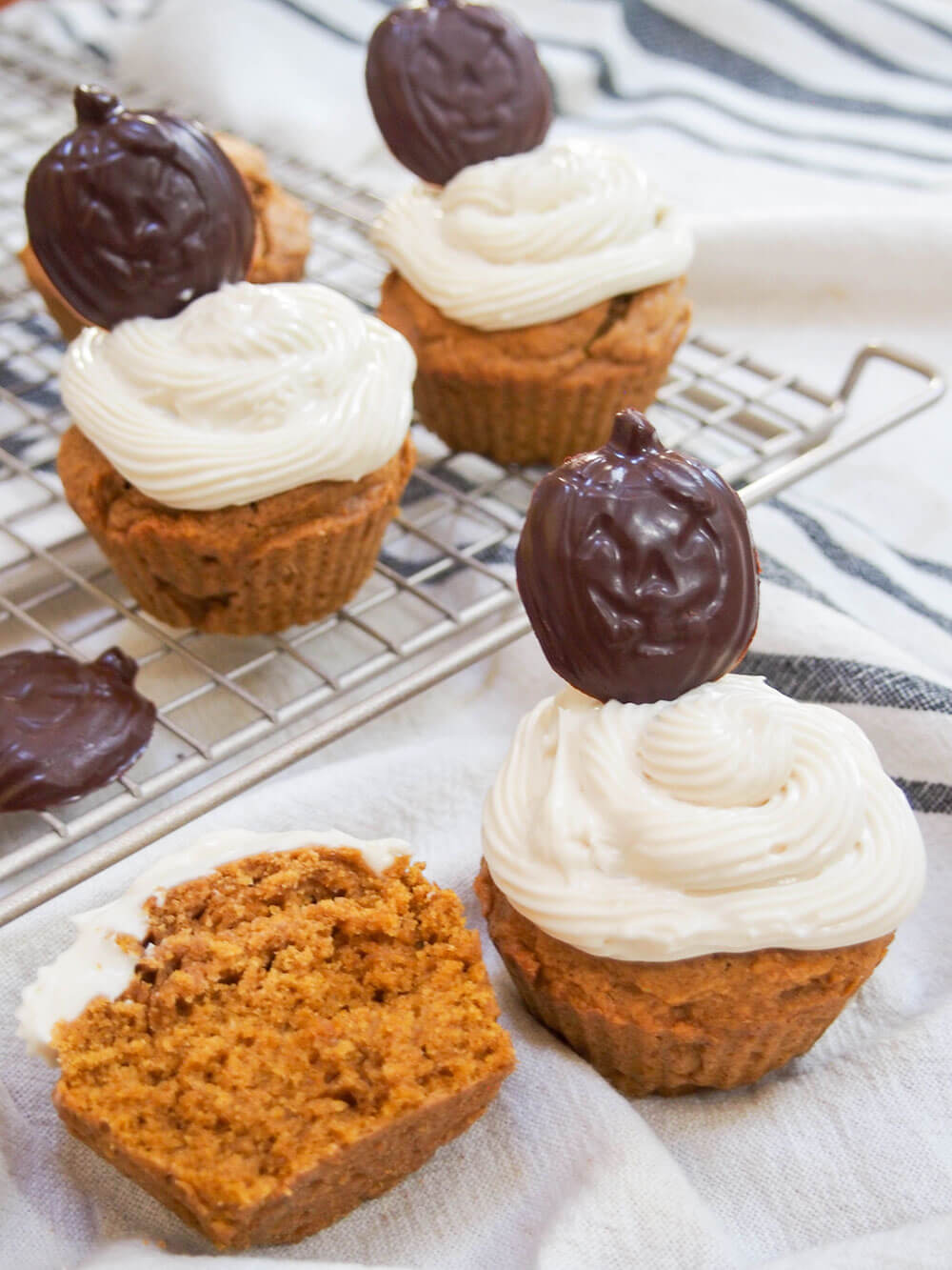 Pumpkin cupcakes with one cut open to side of a whole one topped with chocolate pumpkin topper