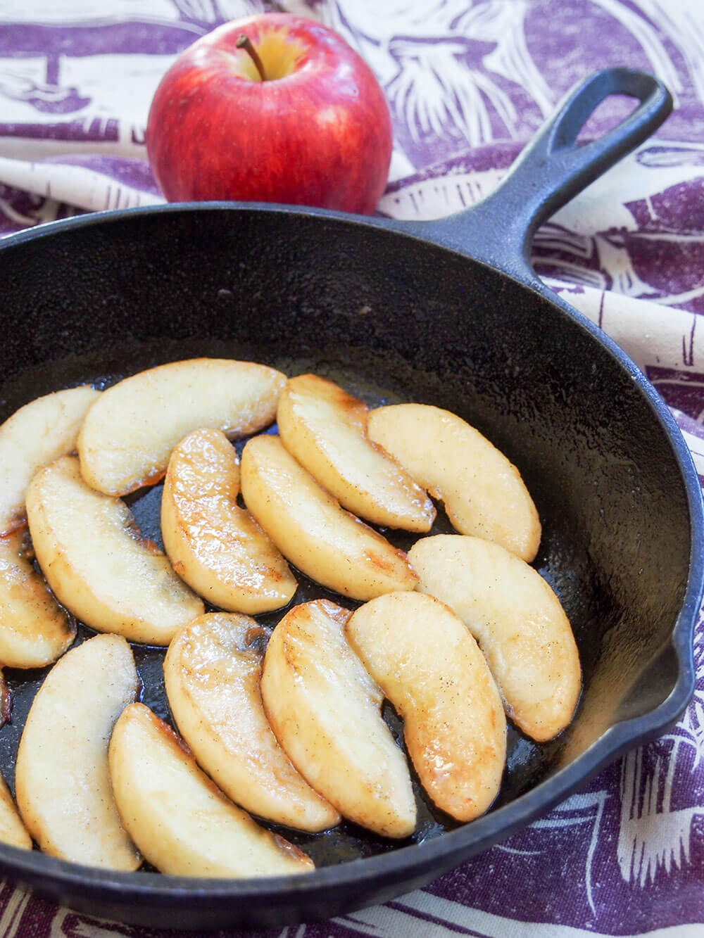 side view of vanilla fried apples in skillet with apple behind