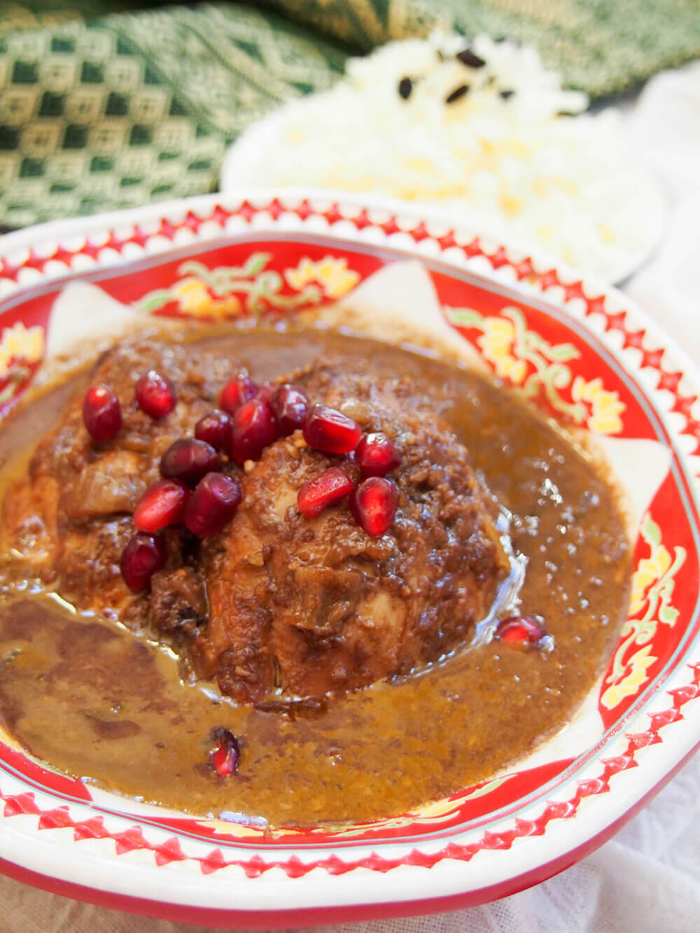 Fesenjan (Persian walnut pomegranate stew) close up on piece of chicken topped with pomegranate arils