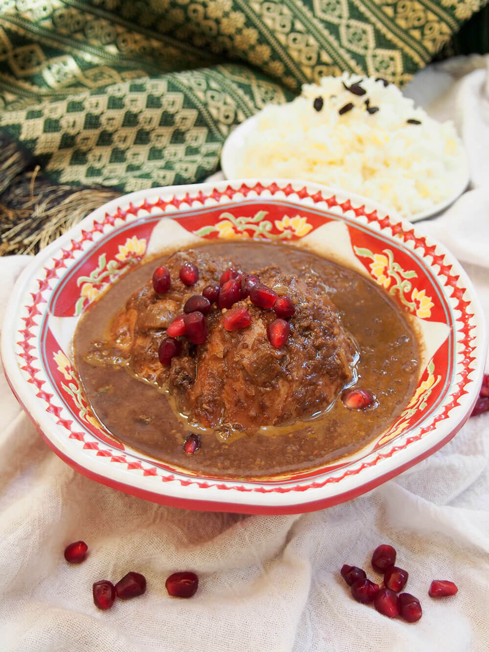Persian walnut pomegranate stew, here made with chicken, served with rice on plate behind