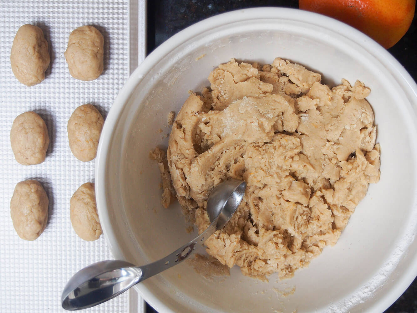 forming melomakarona cookies bowl of cookie dough and formed cookies to side on baking sheet