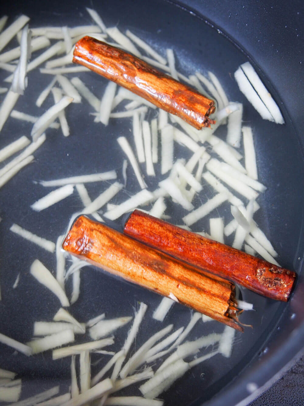 cinnamon sticks and pieces of ginger in pan with water to make tea