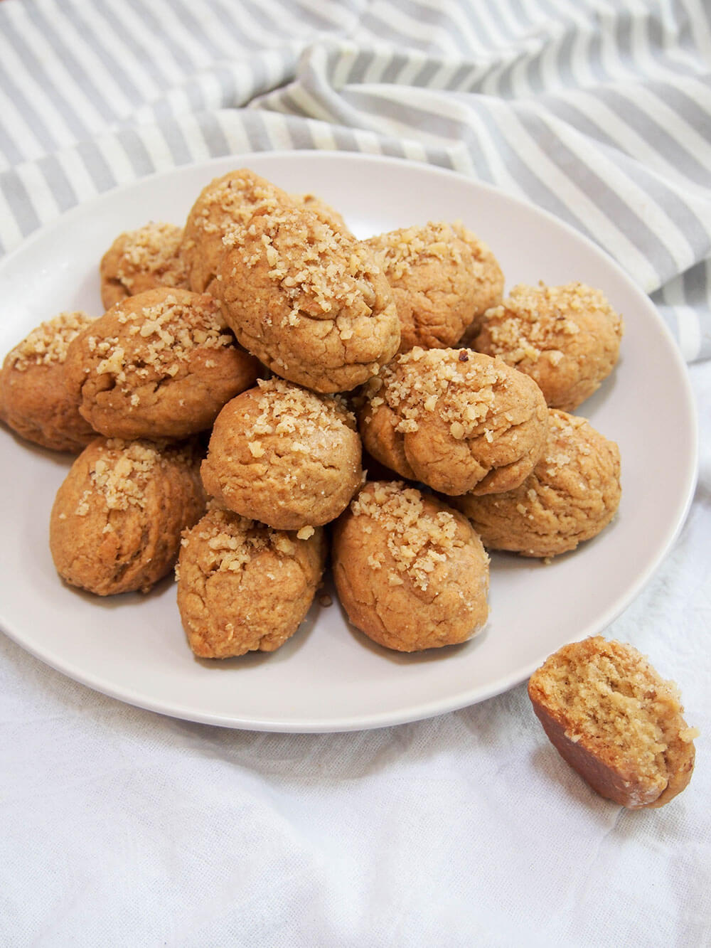 Melomakarona are a classic Greek cookie, with a gently spiced flavor in the dough and finished by dipping them in honey syrup. They're tasty little bites! plate stacked with melomakarona (Greek honey cookies) with one bitten to side