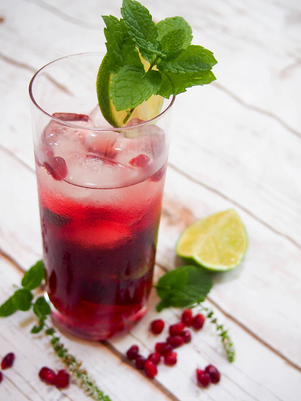 Pomegranate mojito to side with lime, mint and pomegranate seeds around glass