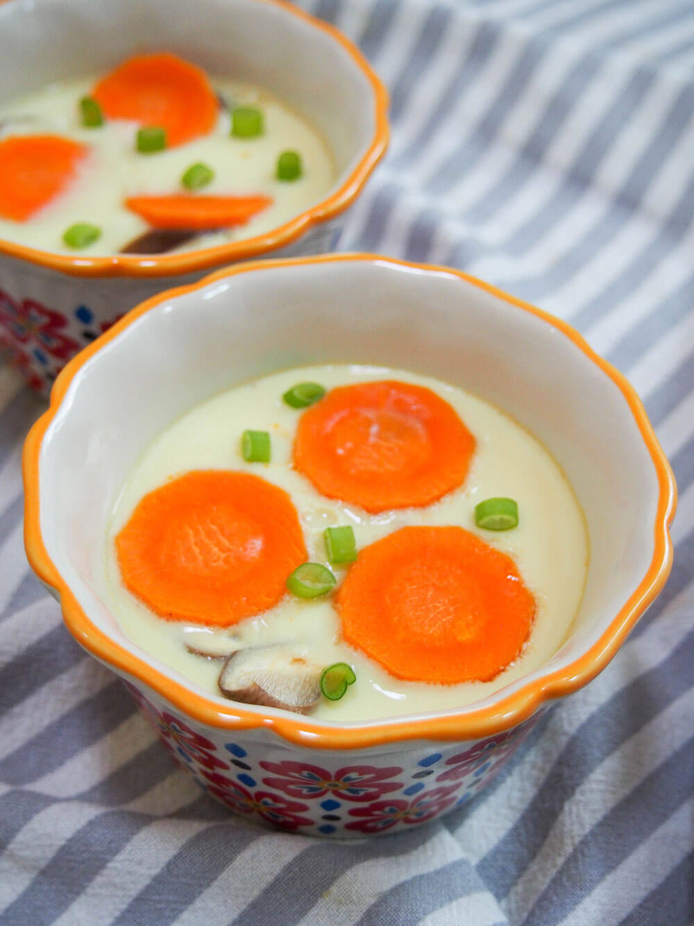 two dishes of chawanmushi - Japanese savory egg custard - topped with carrot and green onion slices