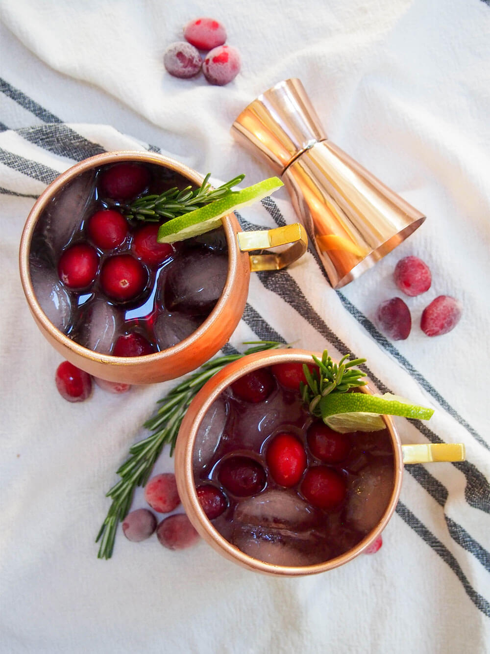 This cranberry Moscow mule is a simple seasonal twist on a classic cocktail, that can also easily be made as a mocktail. mugs of cranberry Moscow mule from overhead with jigger to side