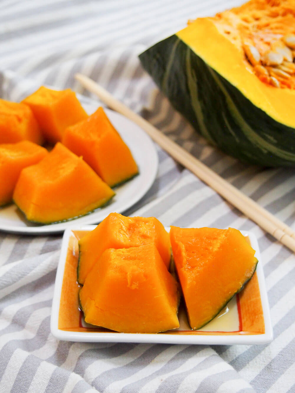 small plate of Japanese simmered kabocha squash in front of larger plate and piece of squash
