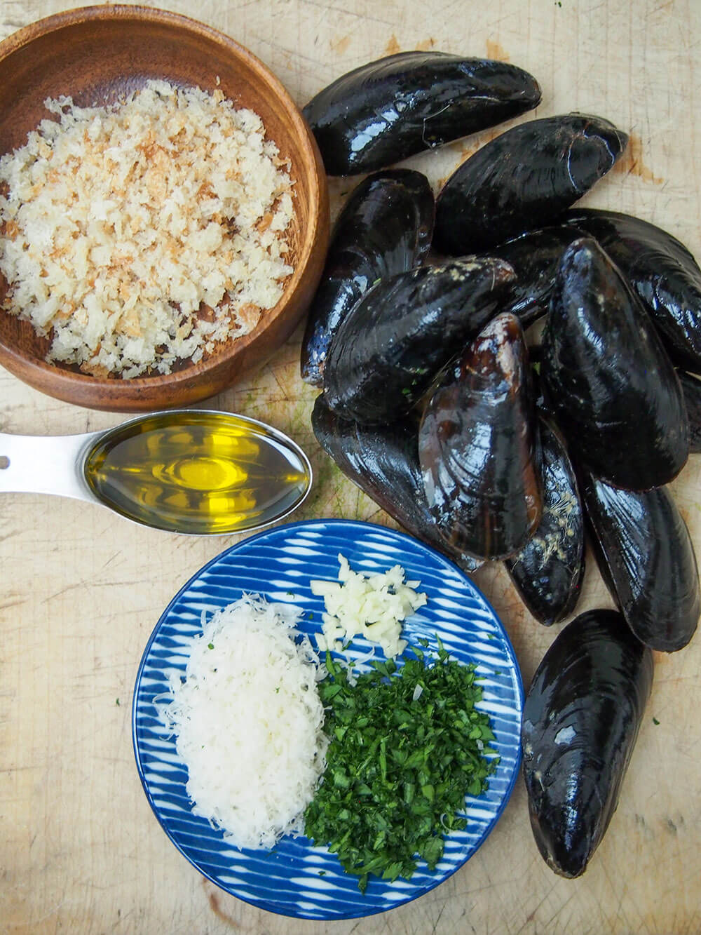 ingredients for baked mussels laid out - mussels, breadcrumbs, oil, parsley, parmesan and garlic