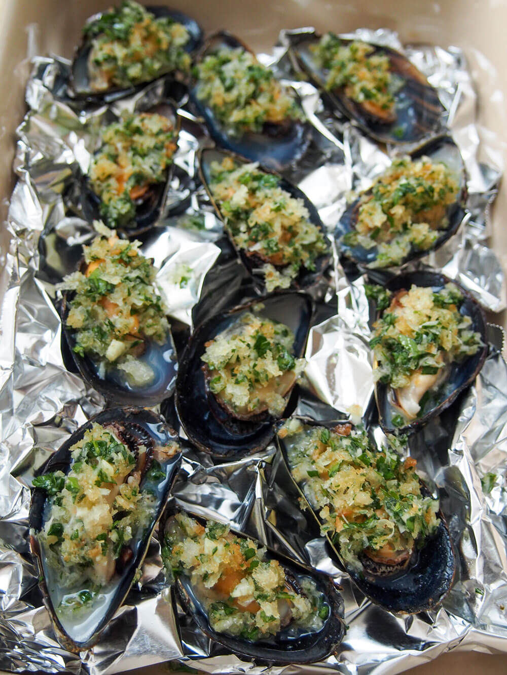 mussels with topping on them, sitting on a bed of scrunched foil, ready to bake