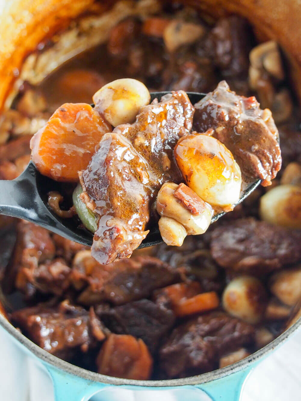 Beef bourguignon with some beef and vegetables on spoon in front of pot