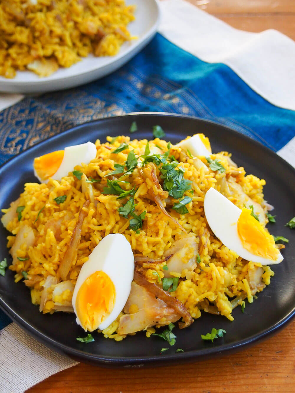 plate of kedgeree on plate, garnished with hard boiled egg and cilantro, with second plate behind