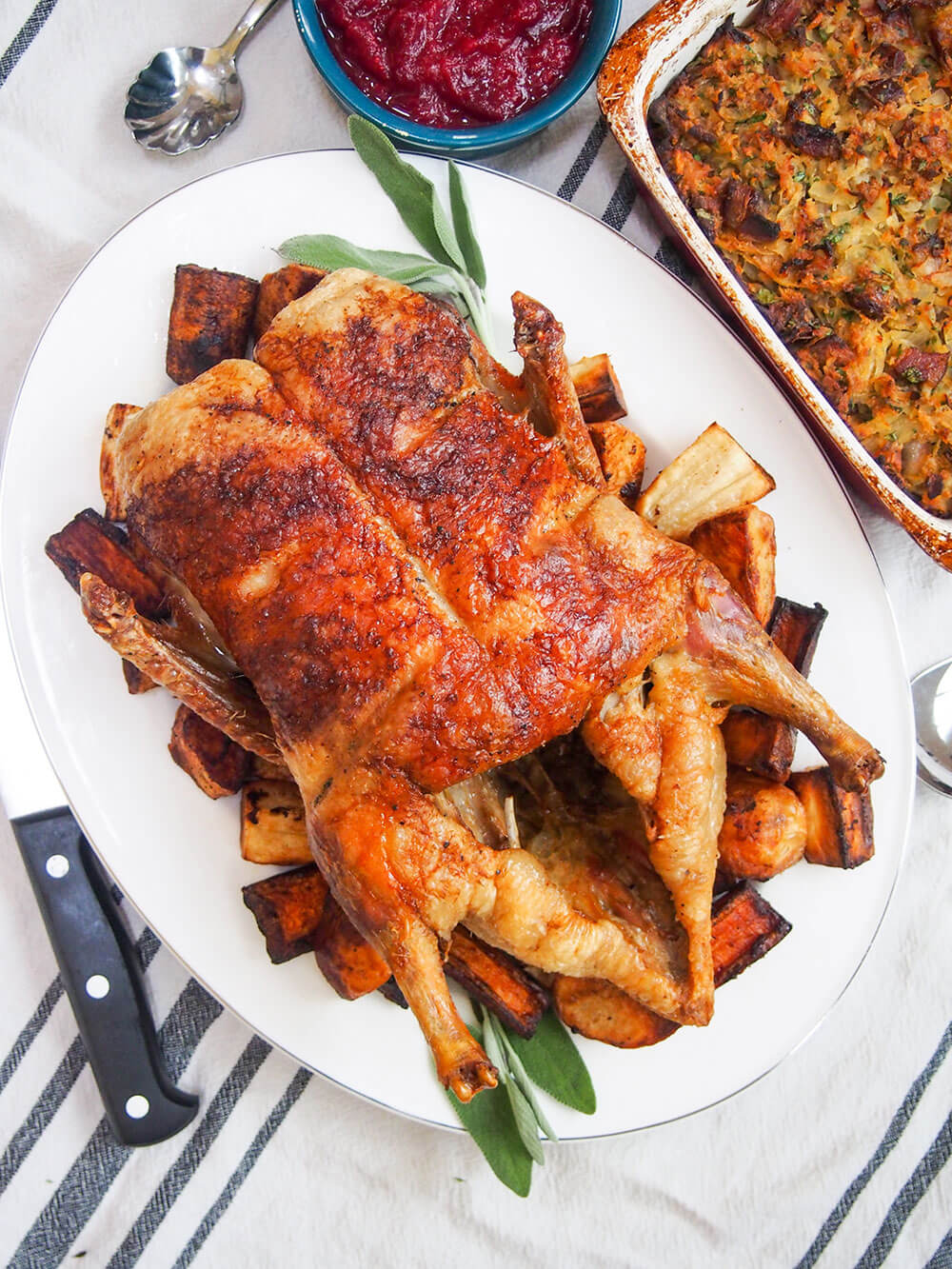 roast duck and vegetables from overhead with knife to one side and dish of stuffing to other