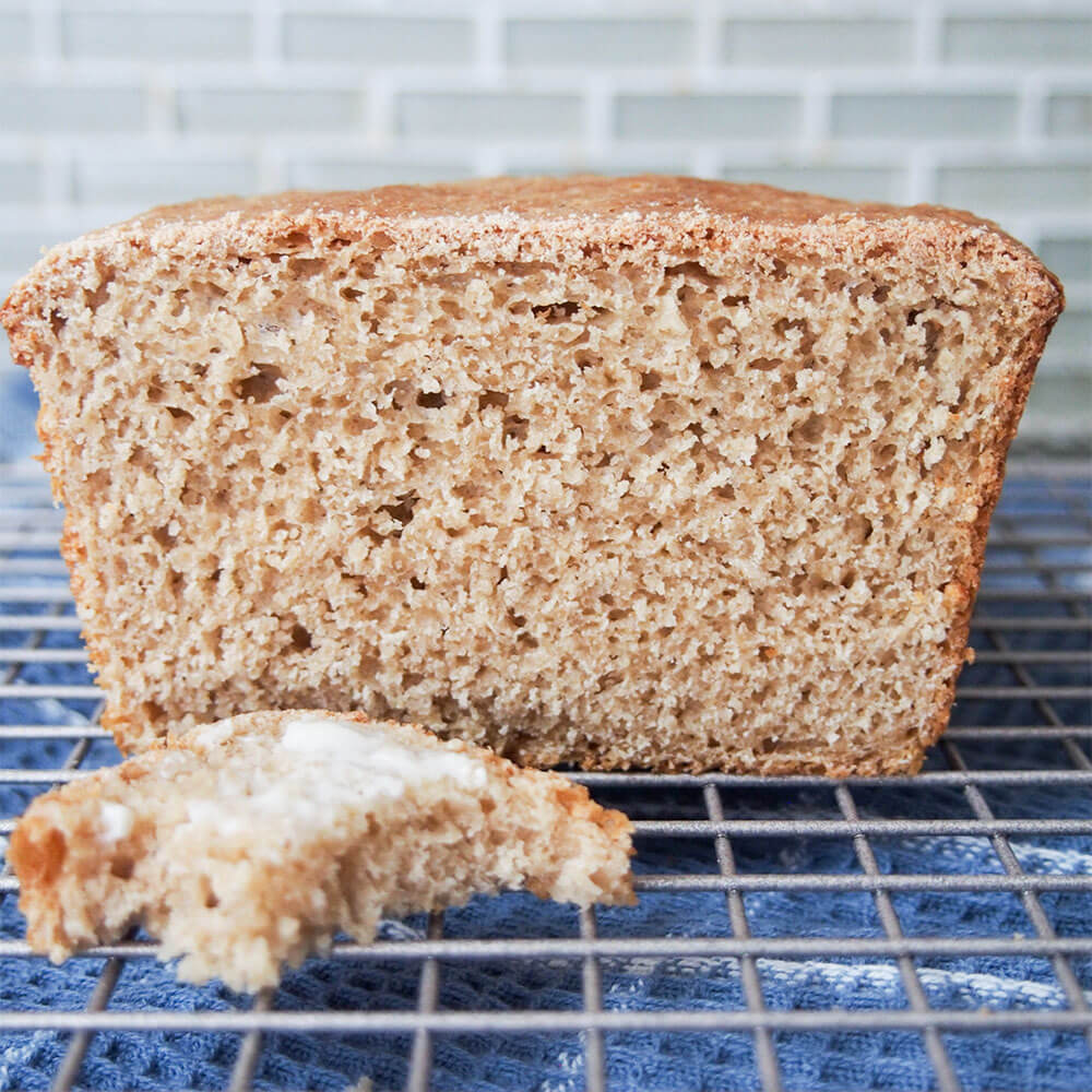 cut sprouted wheat bread loaf viewed from side with small bitten piece in front
