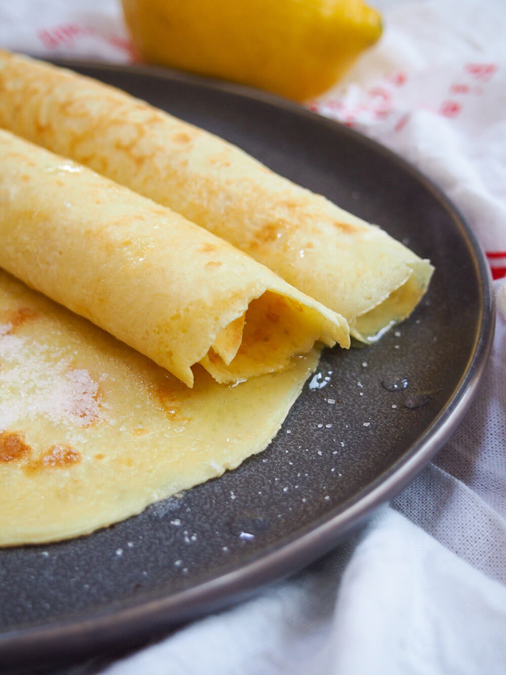 closeup of British pancakes - two rolled on top of another, all with lemon and sugar