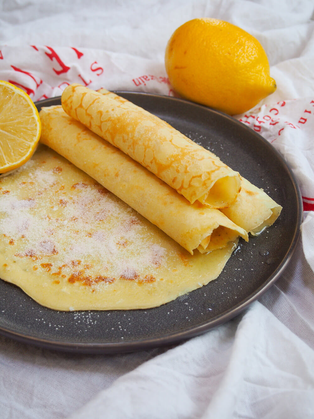 British pancakes on plate, some rolled in stack to side and one on bottom with sugar on top