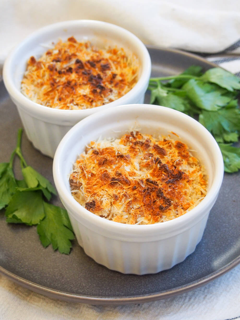 Coquille St Jacques is a scallop gratin with the scallops wrapped in a cream & wine sauce with a crisp topping. Make someone feel special and make it soon! Two dishes filled with coquille St Jacques - scallop gratin - with parsley garnish to side