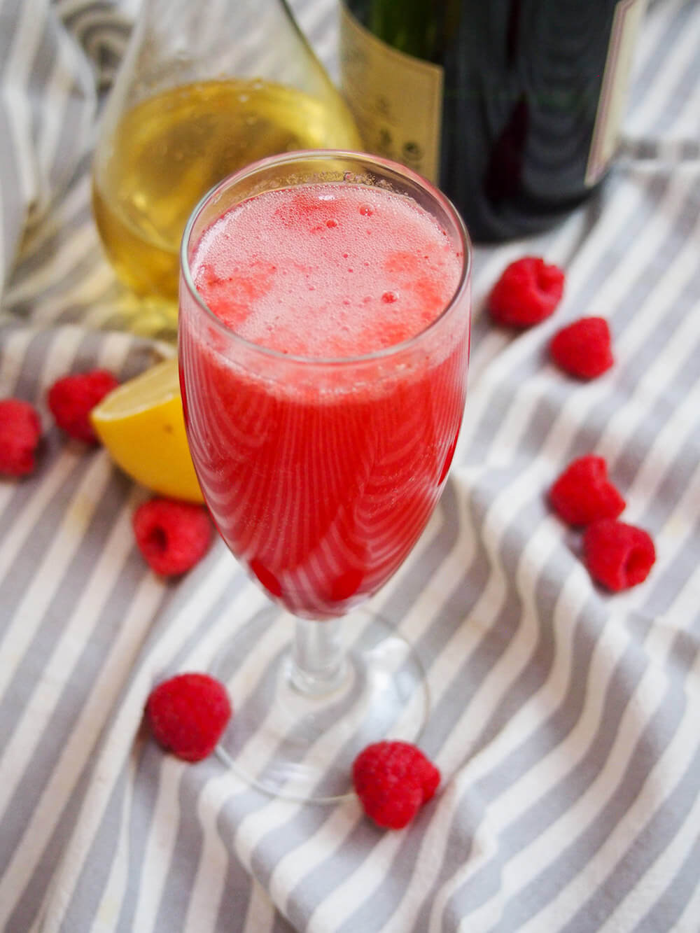 glass of lemon raspberry bellini with raspberries scattered around glass