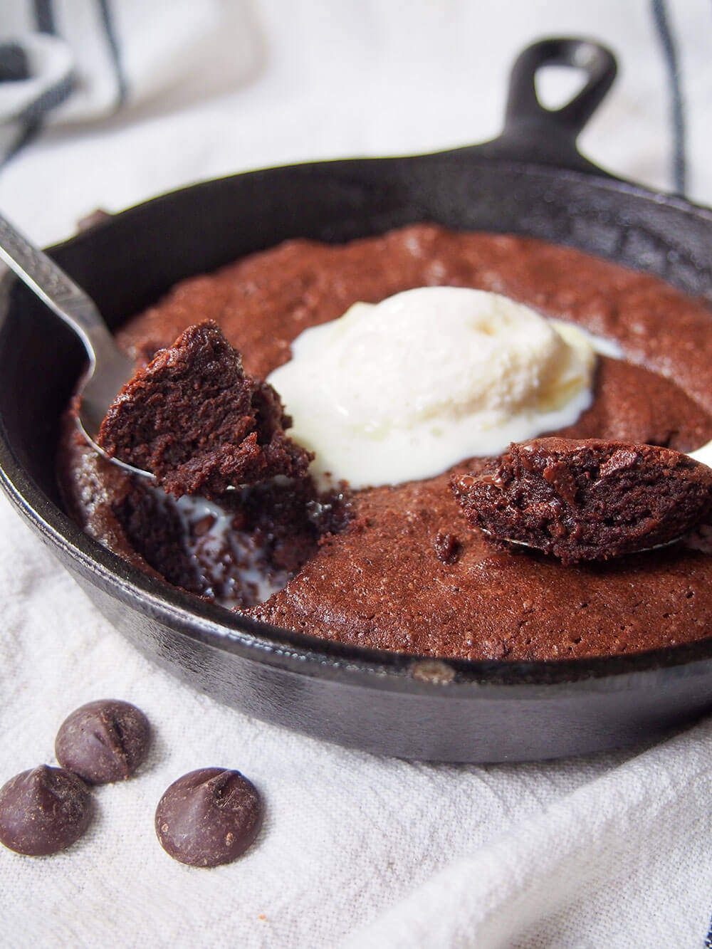 two spoons with spoonfuls of brownie sitting on top of rest, topped with ice cream