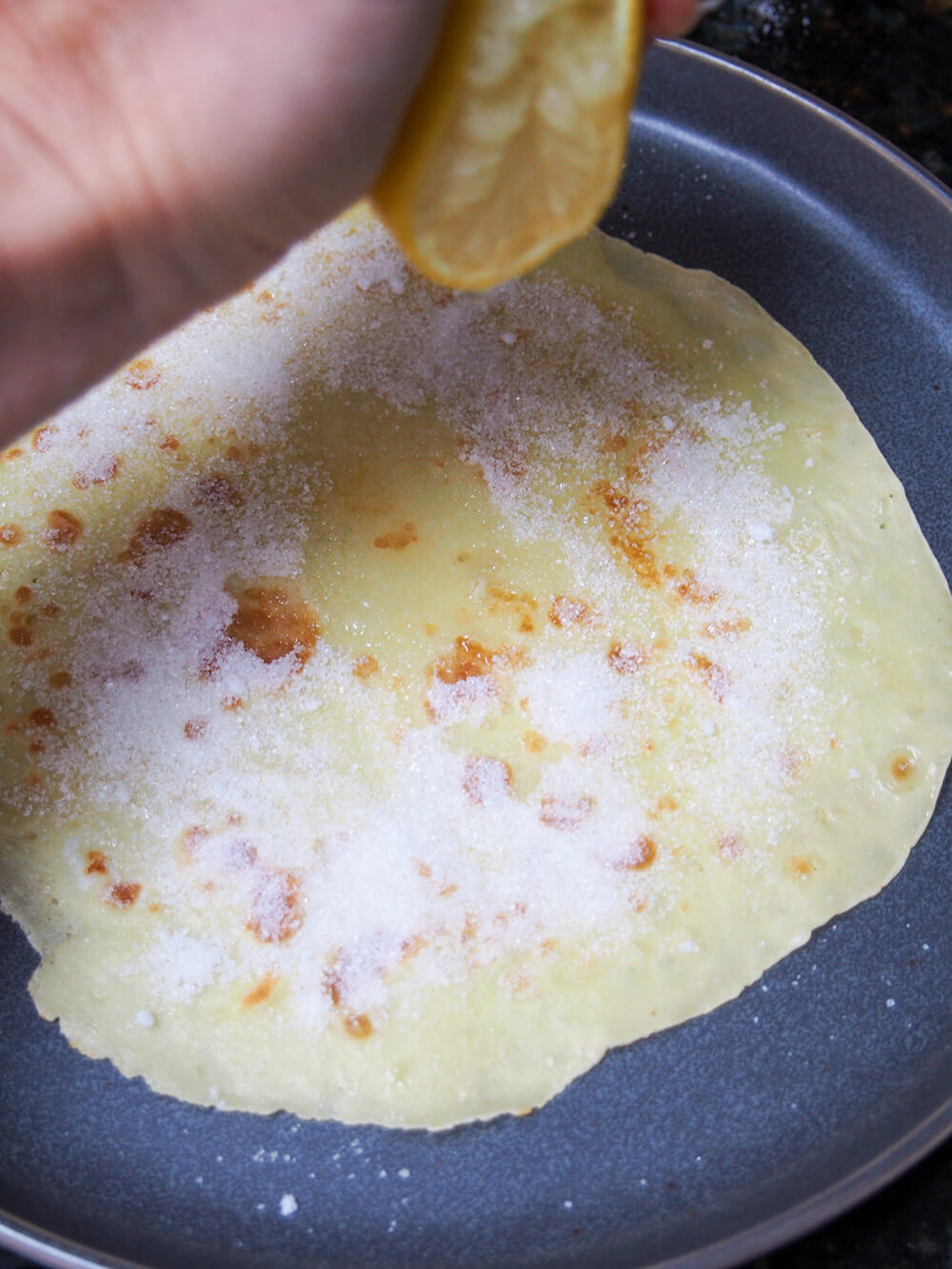 squeezing lemon on pancake, already topped with sugar