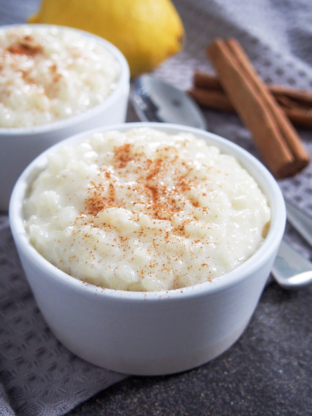 Bowl of arroz con leche with spoons, cinnamon sticks and lemon behind