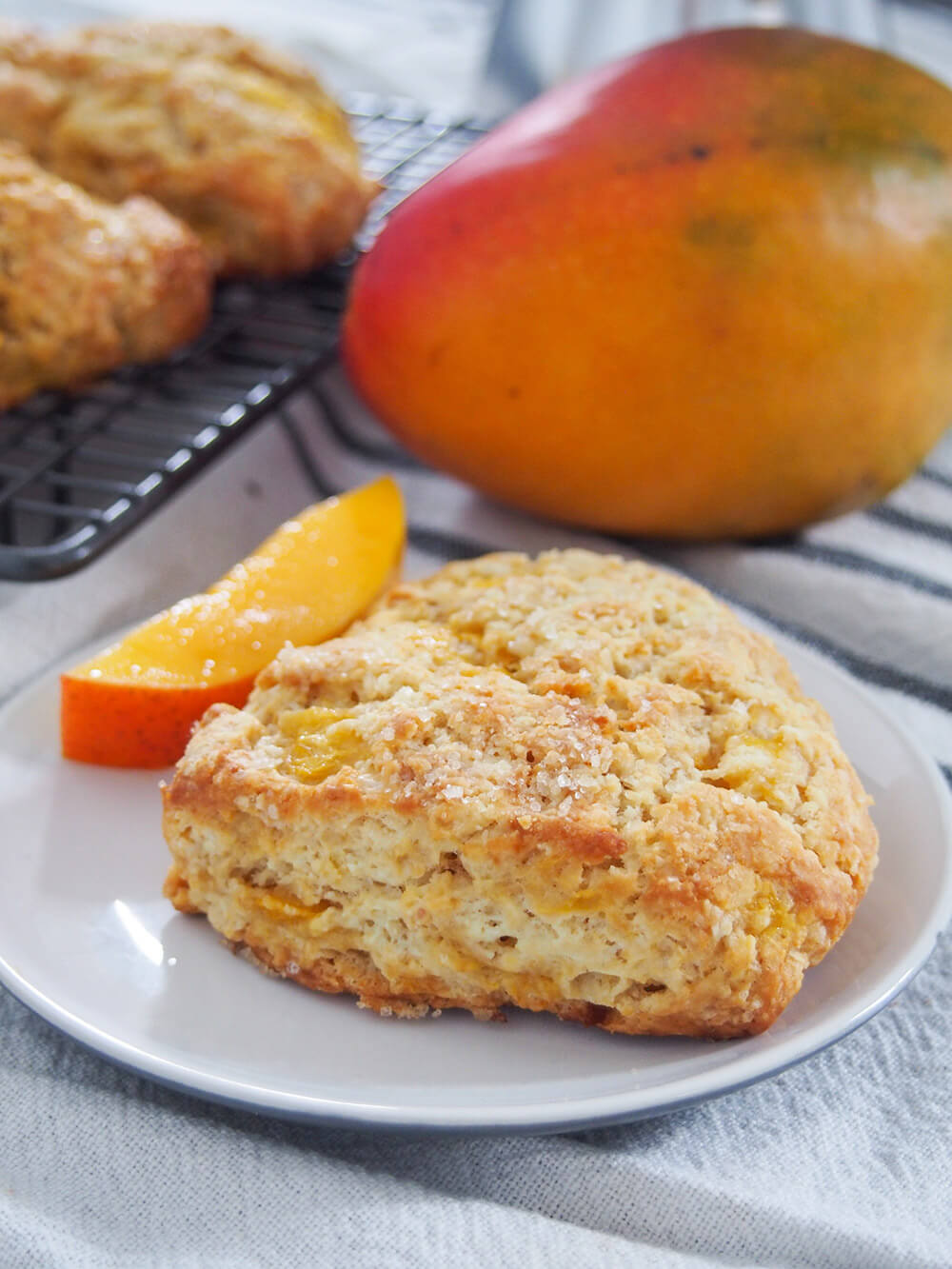 Coconut mango scones with one on plate with mango behind